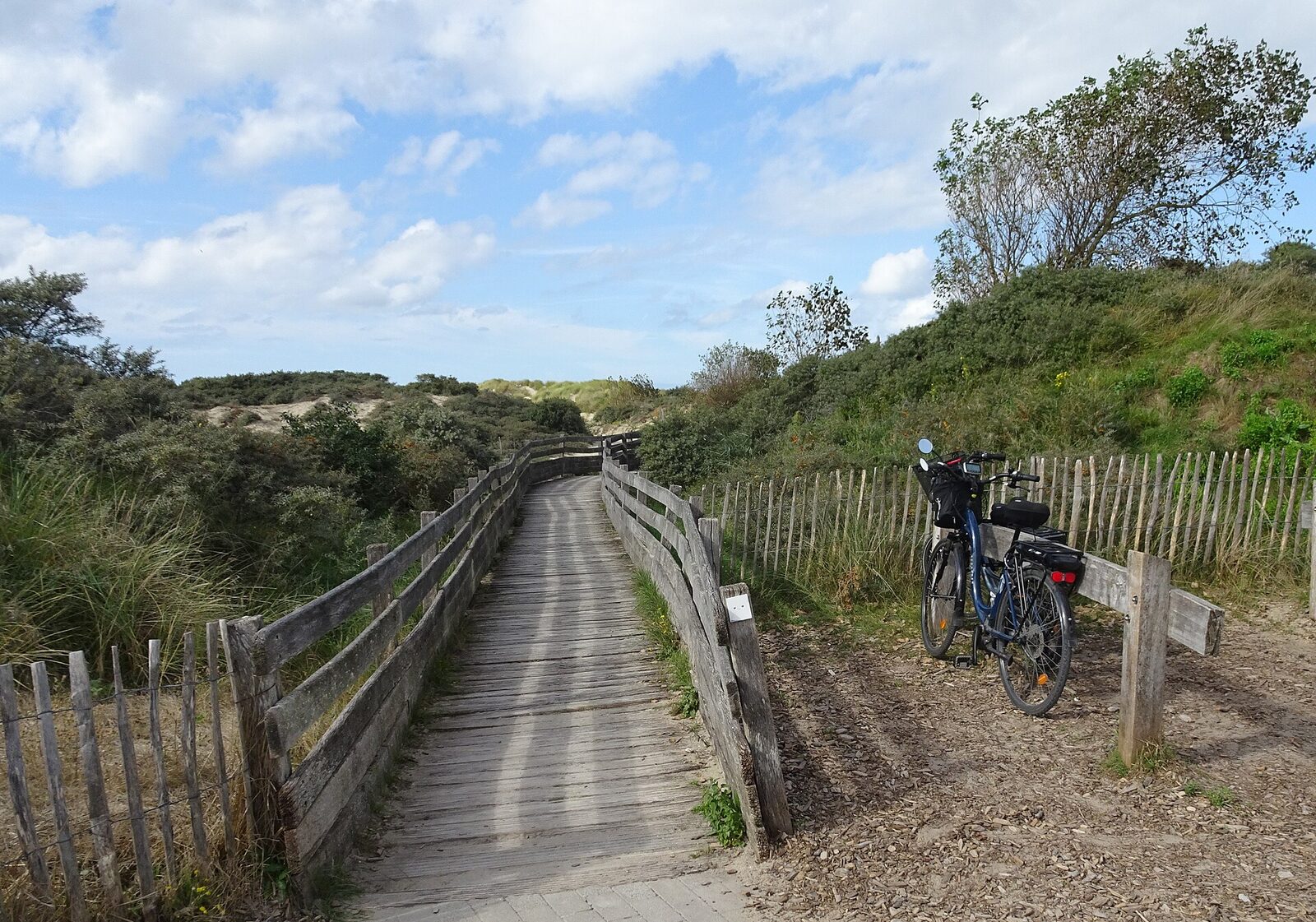 Un vélo garé au bord d’un chemin de planches dans les dunes de l’estuaire de la Canche