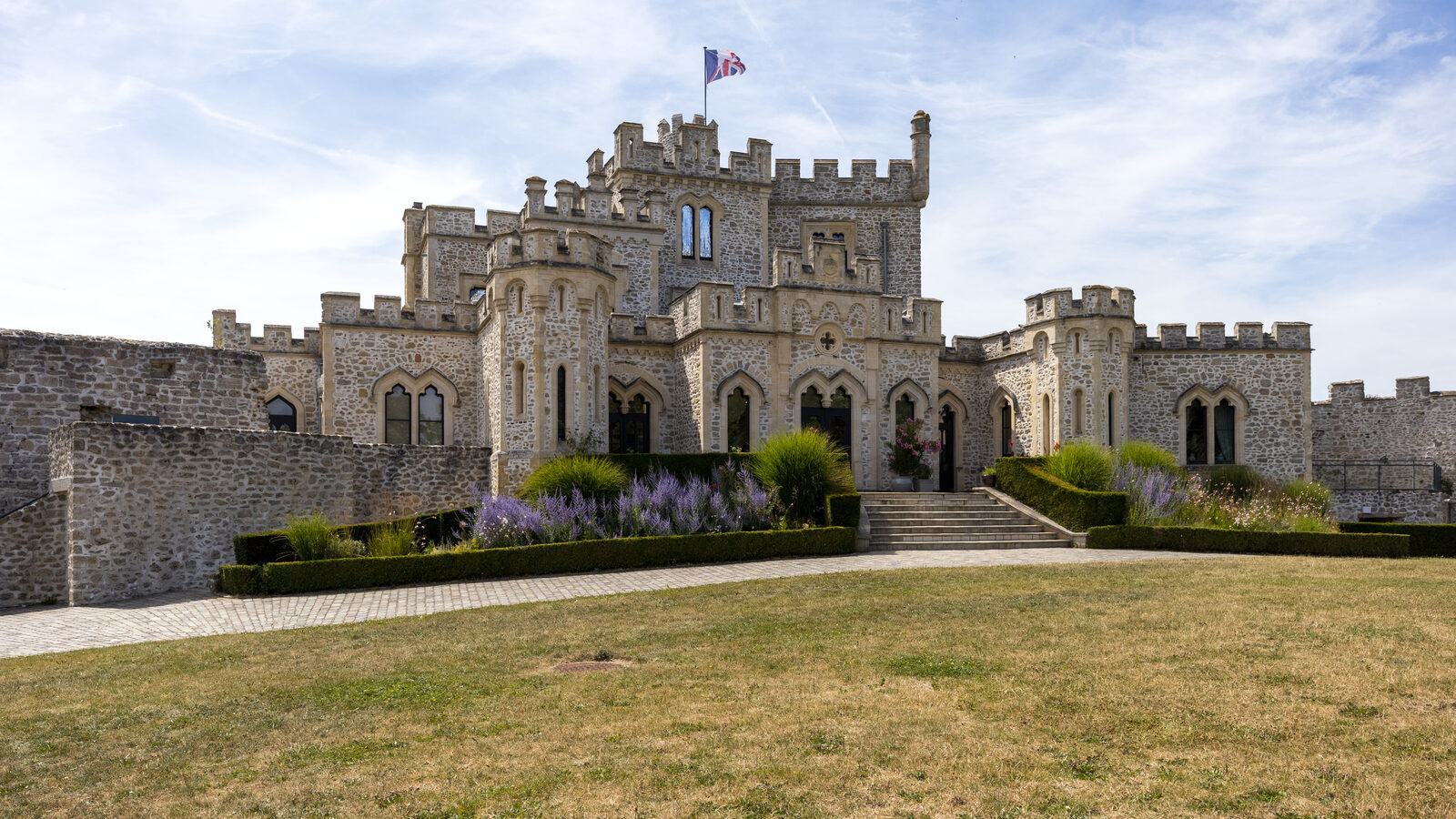 La façade crénelée du château d’Hardelot à Condette, avec son escalier d’entrée, ses massifs de lavande et une pelouse au premier plan