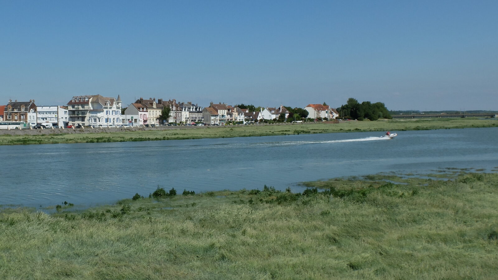 Un petit bateau semi-rigide file sur la Canche à marée haute, devant les maisons des quais d’Étaples