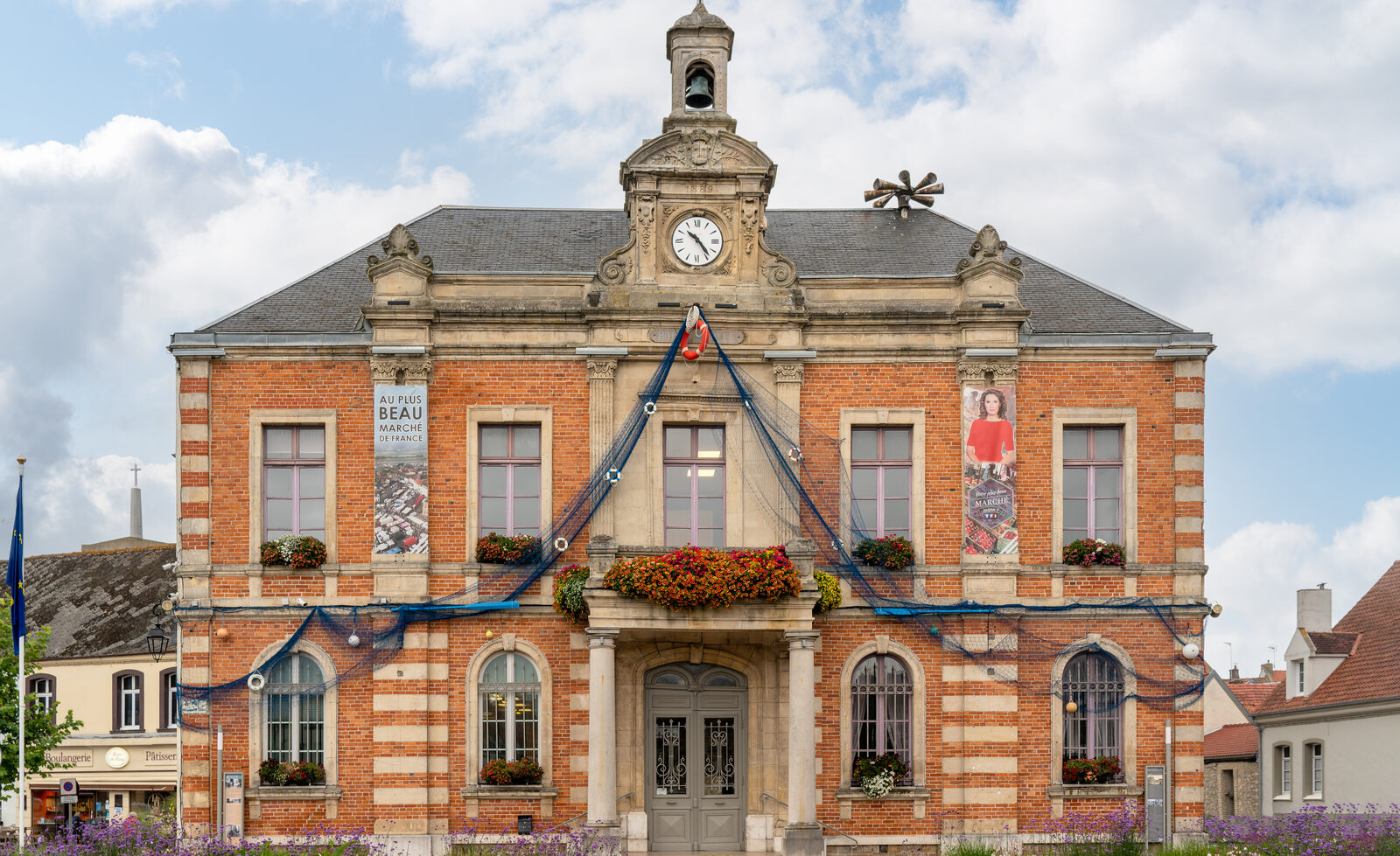 La façade de brique de l’hôtel de ville d’Étaples, place du Général-de-Gaulle, avec une banderole « Au plus beau marché de France » et des filets de pêche tendus sur la façade