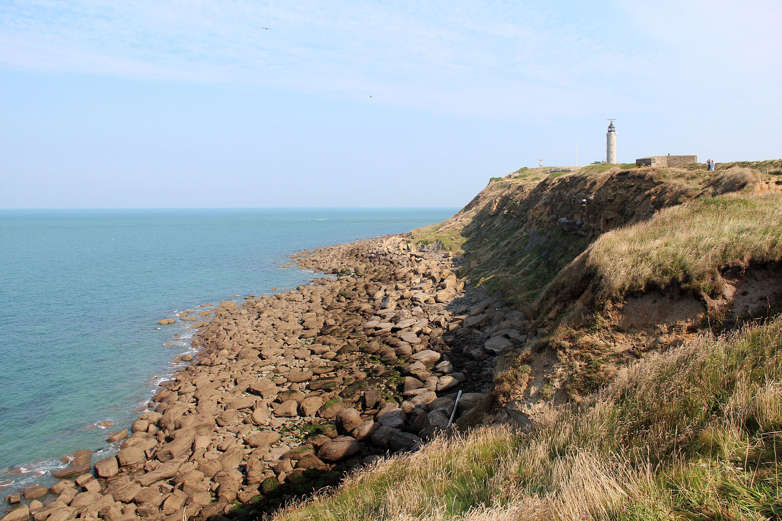 Le phare du cap Gris-Nez au sommet de la falaise, au-dessus d’un rivage de rochers et d’une mer turquoise, par temps ensoleillé