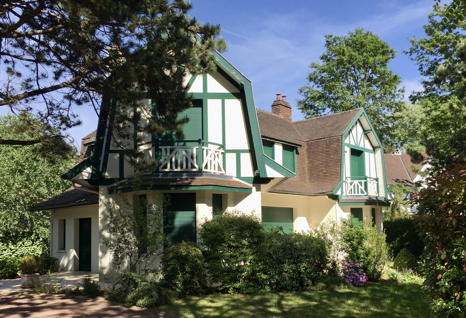 La villa Les Marguerites au Touquet-Paris-Plage, avec ses colombages verts et blancs, entourée de pins et d’arbres sous un ciel bleu